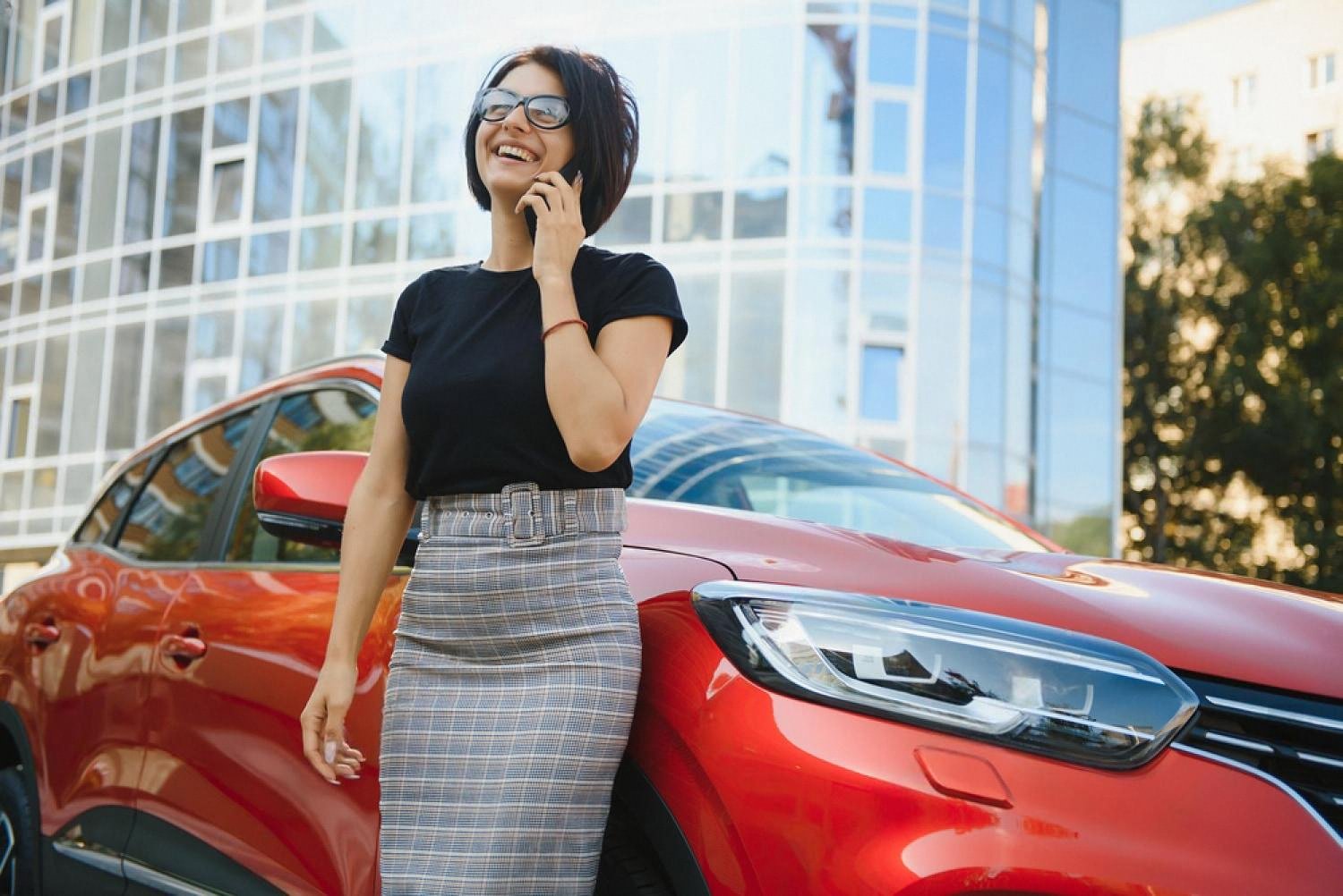 Woman on her phone next to a red rental car after booking online